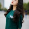 Woman with curly hair and eyeglasses posing outdoors in a green shirt.