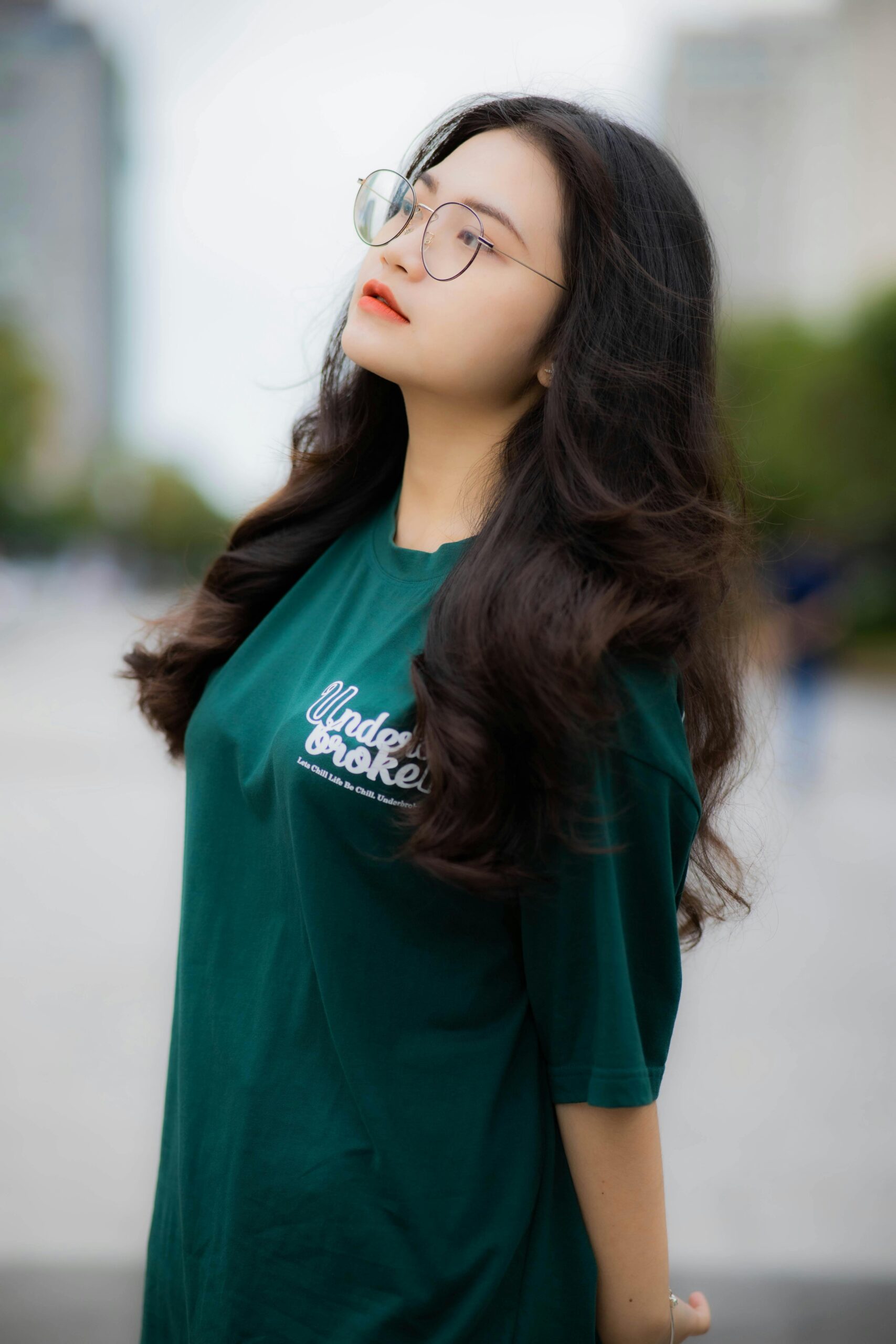 Woman with curly hair and eyeglasses posing outdoors in a green shirt.