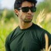A stylish man in sunglasses standing confidently in a sunny field, embracing nature.