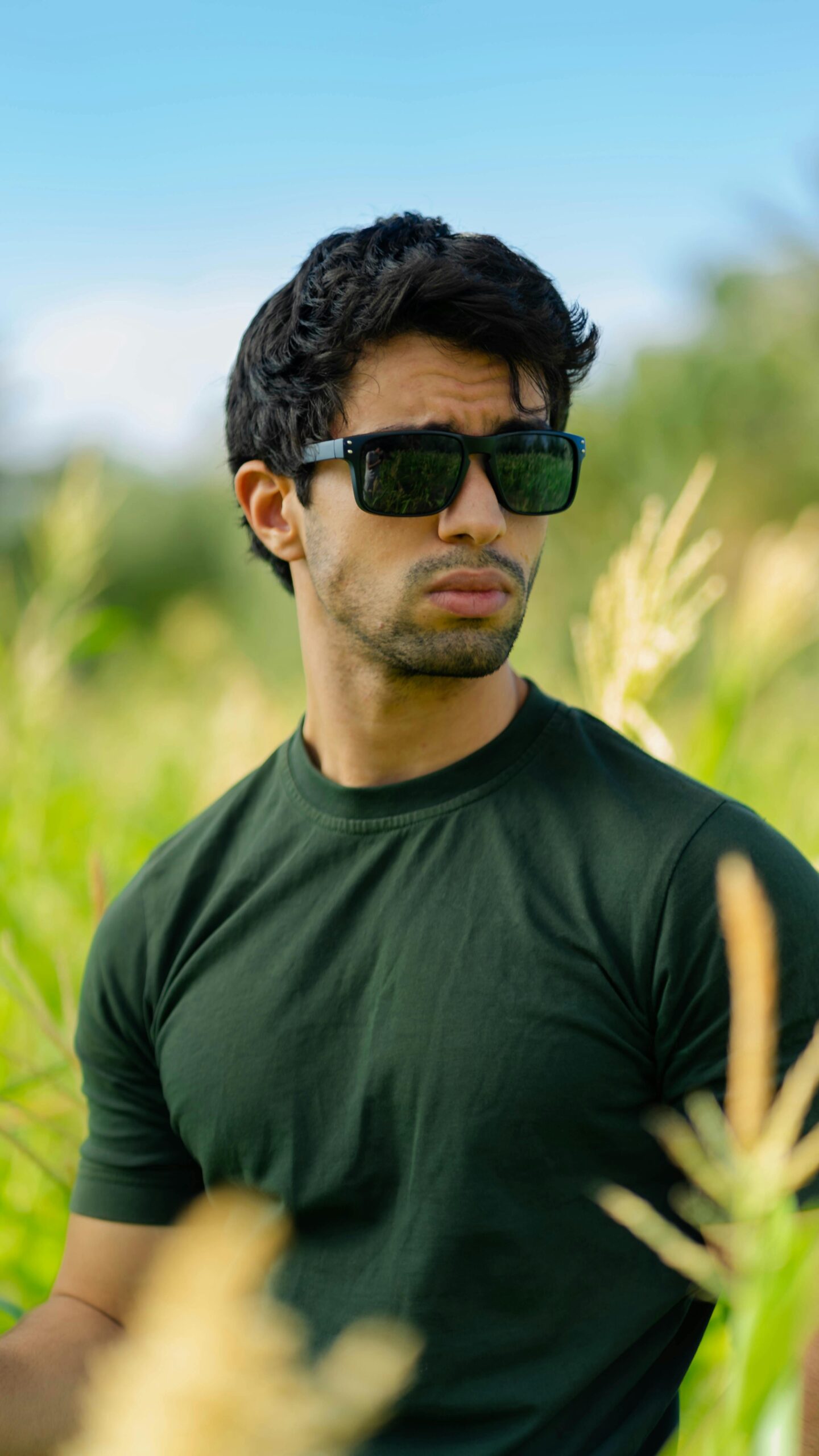 A stylish man in sunglasses standing confidently in a sunny field, embracing nature.